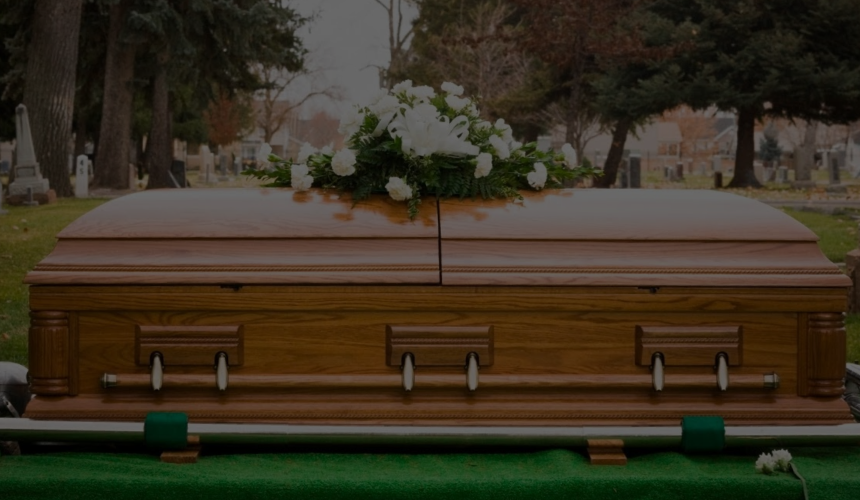Coffin with white flowers on top in a cemetery with trees and gravestones in the background
